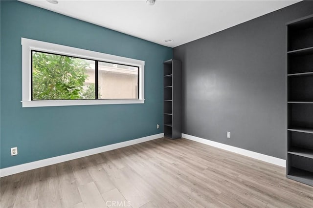 spare room with built in shelves and light wood-type flooring