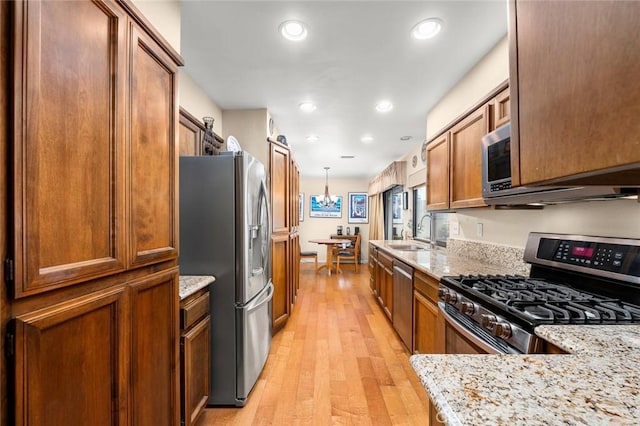 kitchen featuring pendant lighting, sink, light stone counters, stainless steel appliances, and light hardwood / wood-style flooring