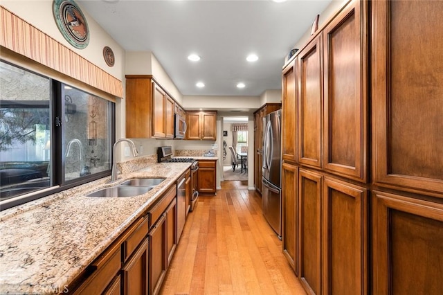 kitchen with light stone counters, appliances with stainless steel finishes, sink, and light wood-type flooring