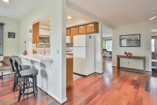 kitchen with hardwood / wood-style floors, white appliances, a breakfast bar area, and sink