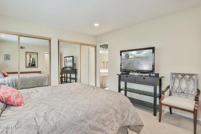 bedroom featuring light carpet, connected bathroom, and two closets