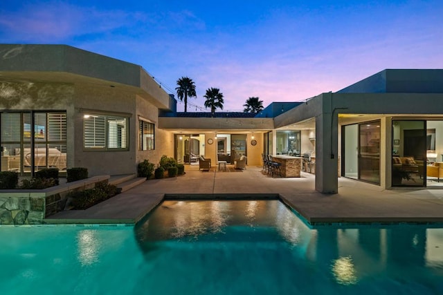 pool at dusk with a patio and exterior bar