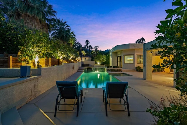 pool at dusk with an in ground hot tub and a patio