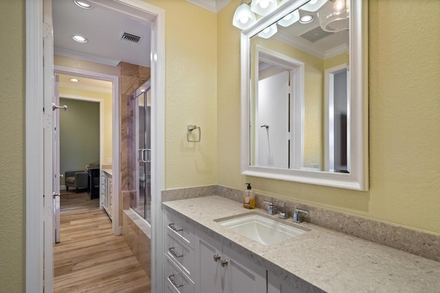 bathroom featuring vanity, wood-type flooring, ornamental molding, and a shower with shower door