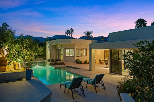 pool at dusk featuring a mountain view and a patio