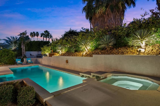 pool at dusk featuring an in ground hot tub