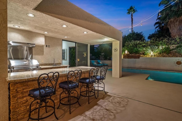 patio terrace at dusk with a grill, exterior kitchen, and an outdoor wet bar