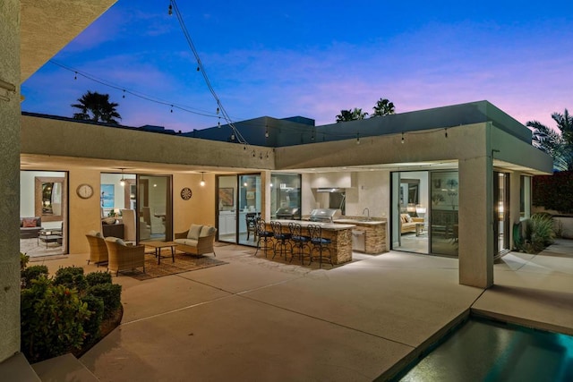 back house at dusk with a patio, an outdoor kitchen, and an outdoor bar