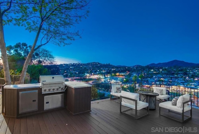 deck at dusk with a mountain view, an outdoor kitchen, grilling area, and a fire pit