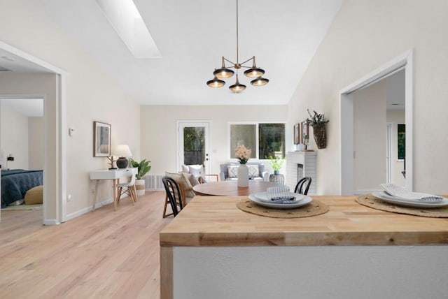 kitchen featuring vaulted ceiling with skylight, pendant lighting, wood counters, a brick fireplace, and light hardwood / wood-style flooring