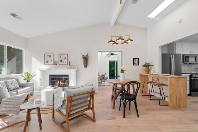 living room with a brick fireplace, vaulted ceiling with skylight, and light hardwood / wood-style floors