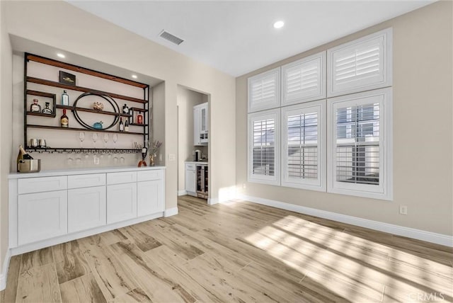 bar with beverage cooler, light hardwood / wood-style floors, and white cabinets