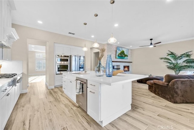 kitchen with hanging light fixtures, stainless steel appliances, a fireplace, a kitchen island with sink, and white cabinets