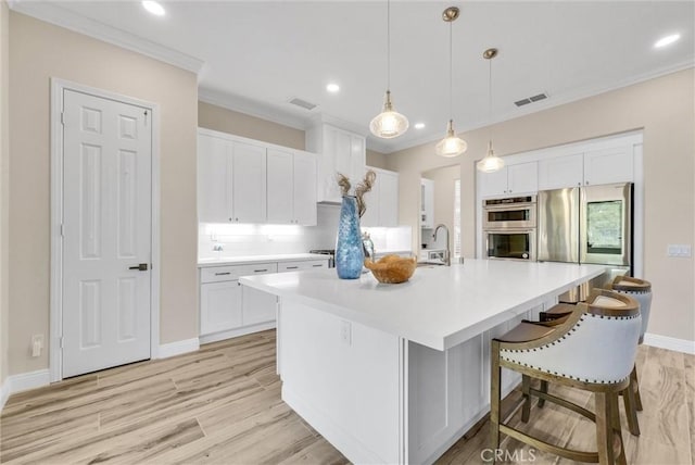 kitchen with crown molding, white cabinetry, hanging light fixtures, stainless steel appliances, and a center island with sink