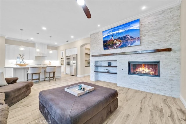 living room featuring ceiling fan, ornamental molding, a stone fireplace, and light hardwood / wood-style flooring