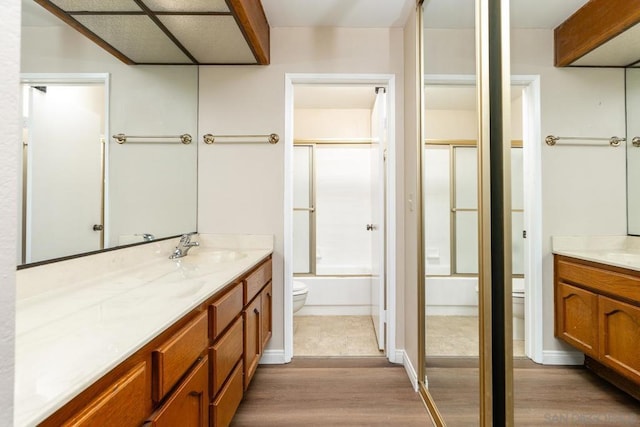 full bathroom featuring vanity, hardwood / wood-style flooring, combined bath / shower with glass door, and toilet