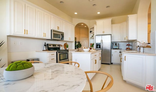 kitchen with sink, appliances with stainless steel finishes, a center island, light stone countertops, and white cabinets