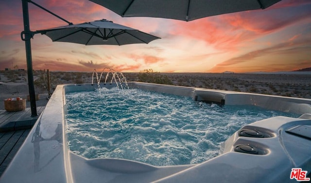 pool at dusk with a hot tub