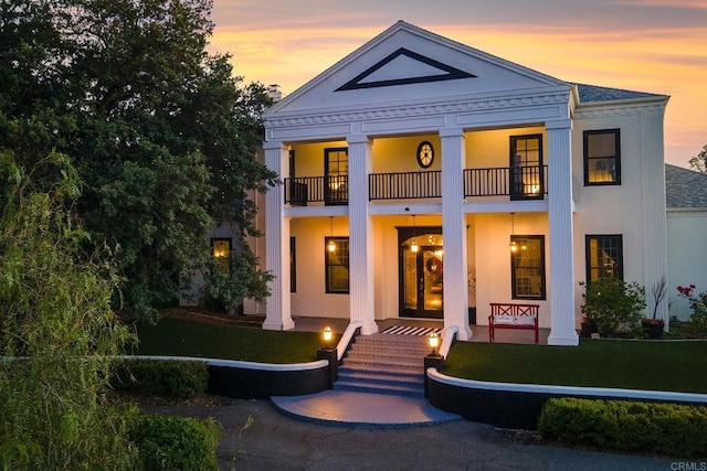 neoclassical home featuring a balcony and a lawn