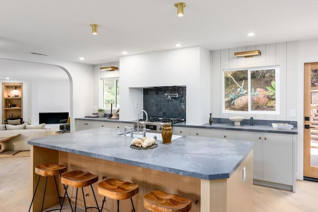 kitchen featuring a breakfast bar area, a kitchen island with sink, dark stone counters, light hardwood / wood-style floors, and white cabinets