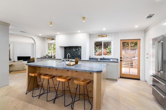 kitchen featuring a spacious island, high end fridge, a breakfast bar area, white cabinetry, and light hardwood / wood-style flooring