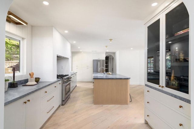 kitchen with sink, appliances with stainless steel finishes, a kitchen island with sink, light hardwood / wood-style floors, and white cabinets