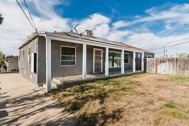 back of house with a chimney, roof mounted solar panels, fence, and stucco siding