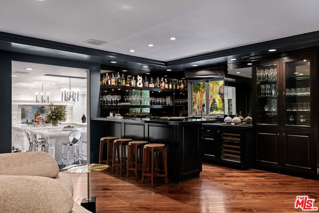 bar with wine cooler, hanging light fixtures, a notable chandelier, and wood-type flooring