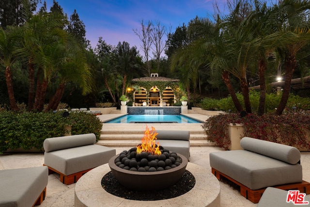 pool at dusk with a patio area and a fire pit