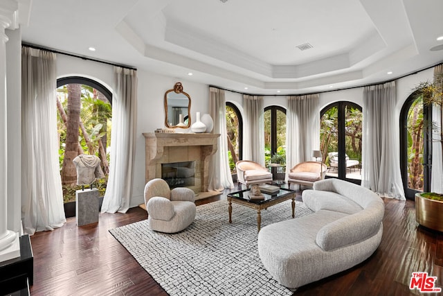 sitting room featuring dark wood-type flooring, decorative columns, a raised ceiling, and a healthy amount of sunlight