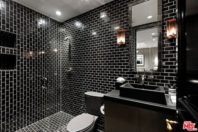 bathroom with vanity, a tile shower, tile walls, and toilet