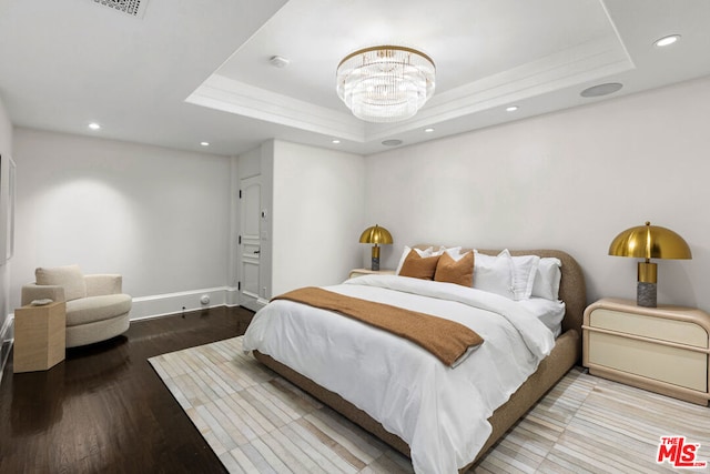 bedroom featuring a raised ceiling, wood-type flooring, and an inviting chandelier