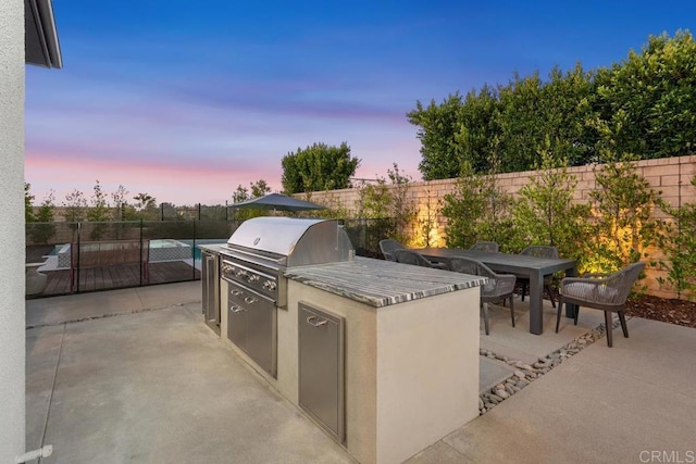 patio terrace at dusk featuring area for grilling and exterior kitchen