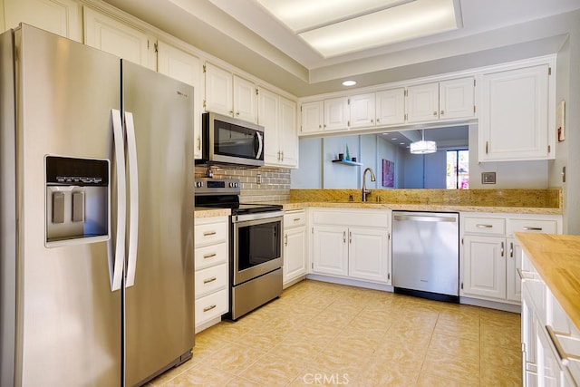 kitchen with sink, appliances with stainless steel finishes, white cabinetry, decorative backsplash, and decorative light fixtures