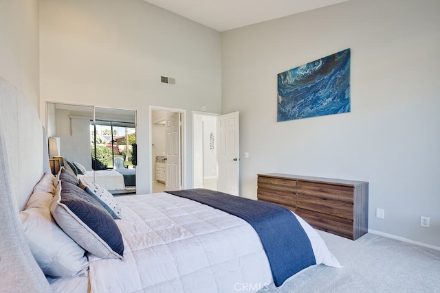 bedroom featuring ensuite bathroom, a towering ceiling, and light colored carpet