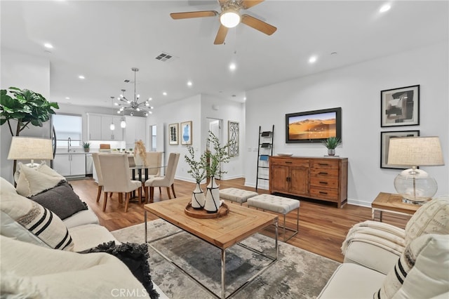 living room with sink, ceiling fan with notable chandelier, and light wood-type flooring