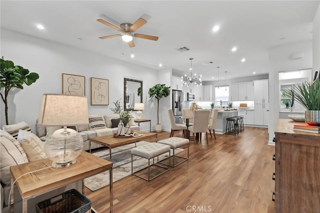 living room with ceiling fan with notable chandelier and light hardwood / wood-style flooring