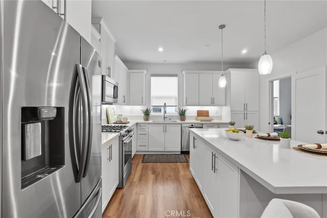 kitchen featuring sink, wood-type flooring, decorative light fixtures, appliances with stainless steel finishes, and white cabinets