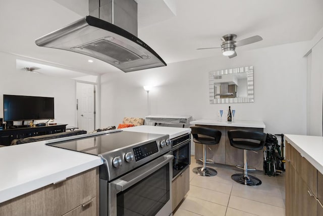 kitchen with stainless steel range with electric stovetop, light tile patterned floors, ceiling fan, and island exhaust hood