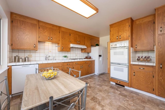 kitchen with backsplash, white appliances, and sink