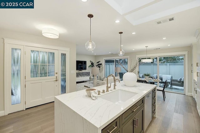 kitchen featuring a kitchen island with sink, hanging light fixtures, light stone countertops, and sink