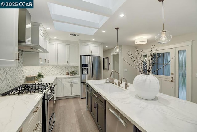 kitchen with appliances with stainless steel finishes, pendant lighting, wall chimney range hood, and sink