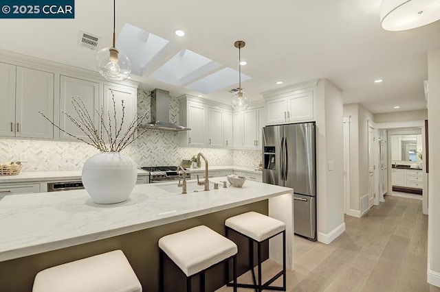 kitchen with appliances with stainless steel finishes, decorative light fixtures, sink, light stone counters, and wall chimney range hood