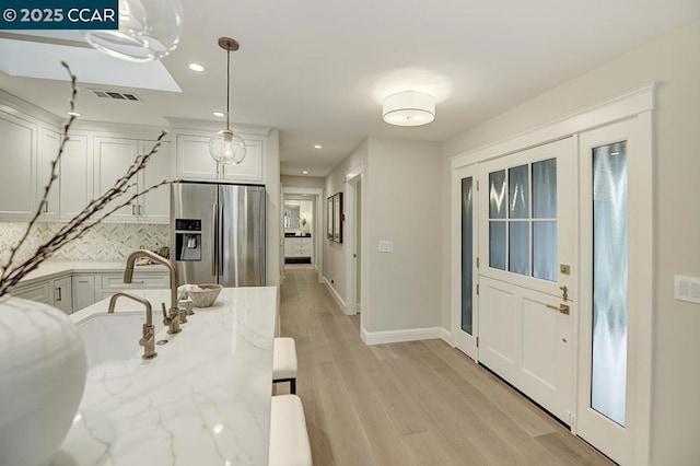 kitchen with sink, white cabinets, hanging light fixtures, light stone counters, and stainless steel refrigerator with ice dispenser