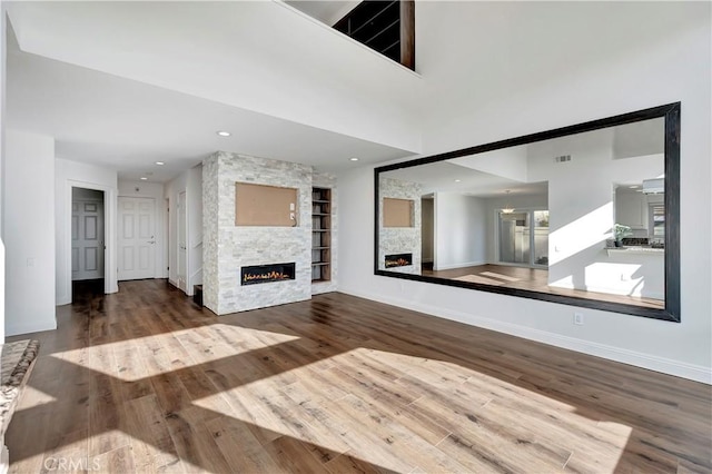 unfurnished living room featuring wood-type flooring, a fireplace, and built in shelves