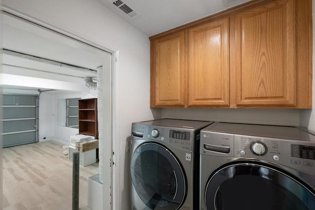 clothes washing area featuring cabinets, separate washer and dryer, and light wood-type flooring