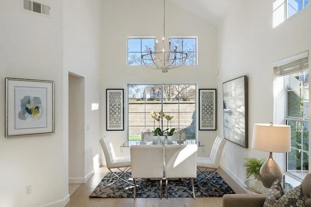 dining room with a towering ceiling, a wealth of natural light, a notable chandelier, and light hardwood / wood-style flooring