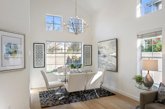 dining area featuring a notable chandelier, hardwood / wood-style flooring, a wealth of natural light, and a towering ceiling