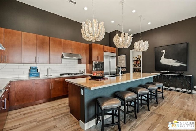 kitchen featuring sink, a breakfast bar area, built in appliances, light hardwood / wood-style flooring, and a kitchen island with sink