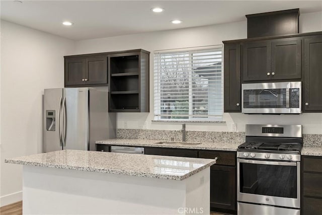 kitchen with light stone counters, appliances with stainless steel finishes, a center island, and sink